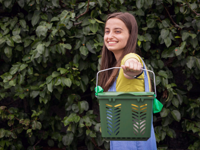 Jente smiler og rekker fram en gr?nn kompostbeholder.