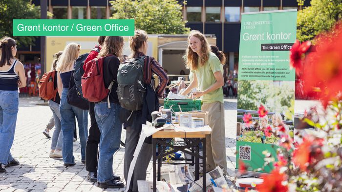 A Green Office stand at Frederikekplassen with Green Office staff talking to students. It's sunny with flowers in the forefront. 