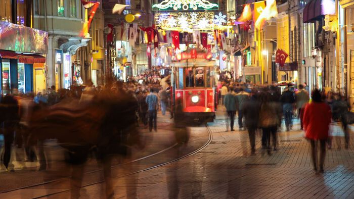 A busy shopping street in the evening, with a tram in the middle, and many people moving and out of focus in the picture. Photo.