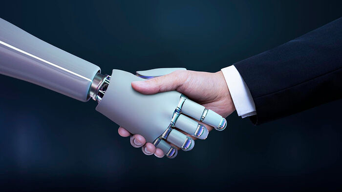 The hand of a robot and the hand of a man wearing a suit giving eachother a handshake. Photo.