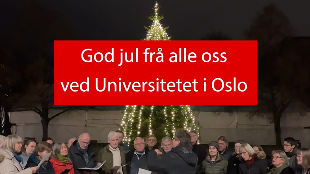 Skjermdump fra film med plakat der det st?r "God jul fra alle oss ved Universitetet i Oslo" med kor og tent juletre i bakgrunn