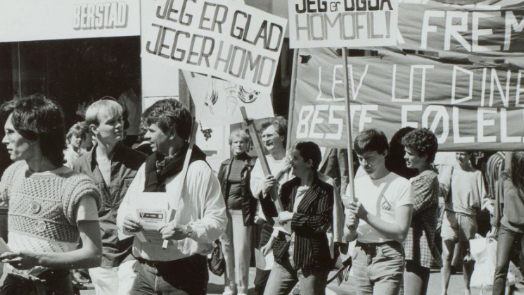 Historisk foto i svart-hvitt fra demonstrasjonstog med paroler som "Jeg er glad jeg er homo"