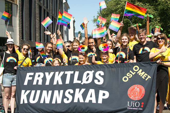 Students and staff from UiO and OsloMet in Pride T-shirts waving Pride flags and holding up the banner "Fearless knowledge"