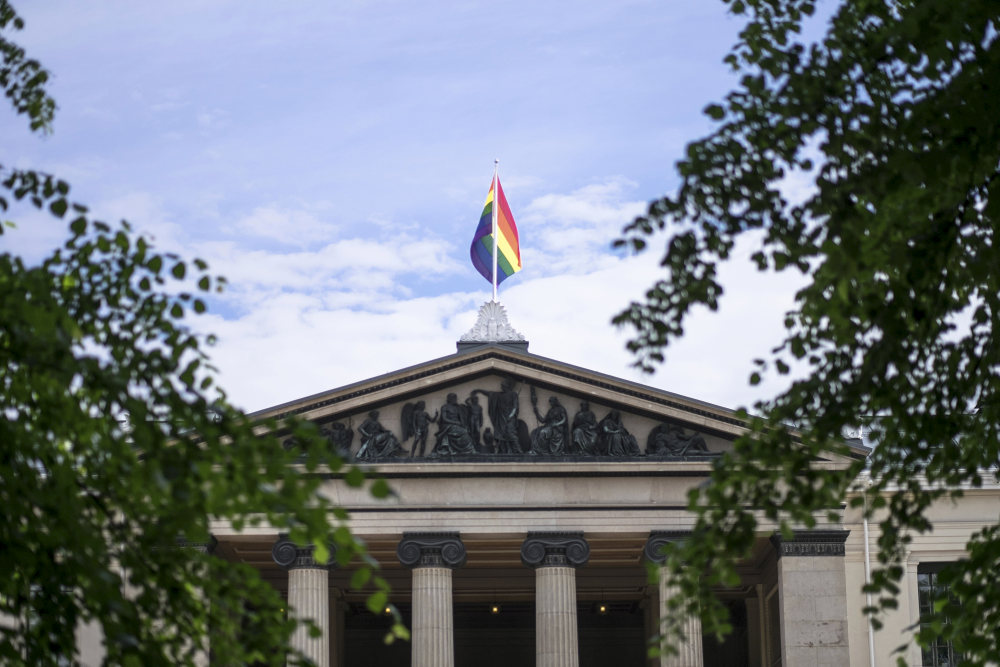 universitetsbygning med Pride-flagg og gr?nn tr?r i forgrunnen