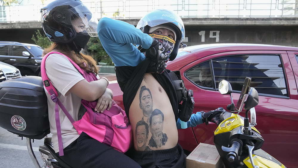 En kvinne og en mann p? moped. Mannen viser tre tatoveringer p? overkroppen, av presidentene Bong Bong Marcos, Rodrigo Duterte og Ferdinand Marcos.