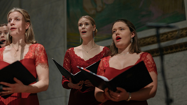 Thee singers in red dresses on the stage in the Aula