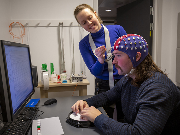 Maja Foldal fester elektroder p? hodet til mann som sitter foran PC-skjerm.
