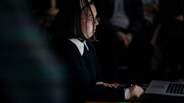 Picture of Alisa Kobzar in a dimly lit room in front of a laptop with people standing around her.