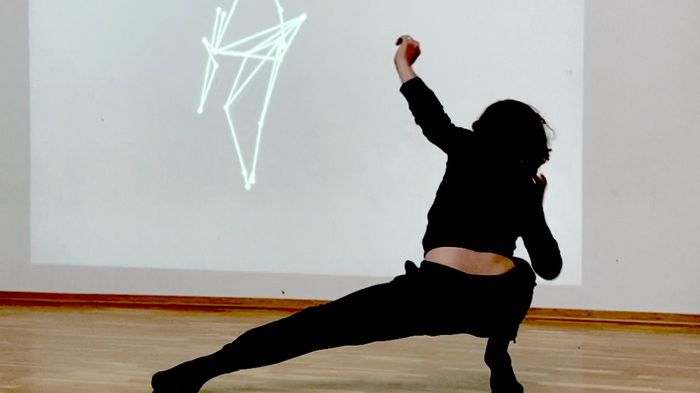 Dancer dancing in the foreground, with an AI image consisting of lines, projected on a screen in the background