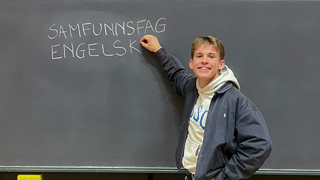 Student st?r foran tavle hvor han har skrevet "SAMFUNNSFAG" og "ENGELSK" med kritt.