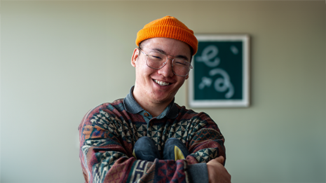 Portrettbilde av student som smiler mot kamera mens han holder klatresko.
