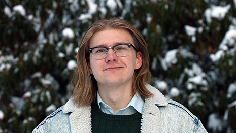 Mannlig student smiler mot kamera foran sn?kledde tr?r