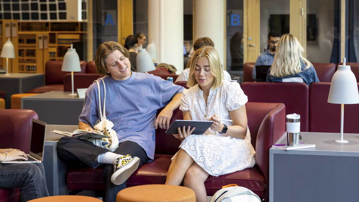 Mann- og kvinnelig student i sofa som ser p? felles iPad