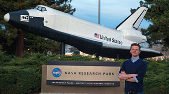 Student foran NASA-skilt og modell av romskip